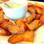 Deep fried wedges of chayote squash on a white square plate. The wedges are surrounding a ramekin dish in the centre, filled with yoghurt.