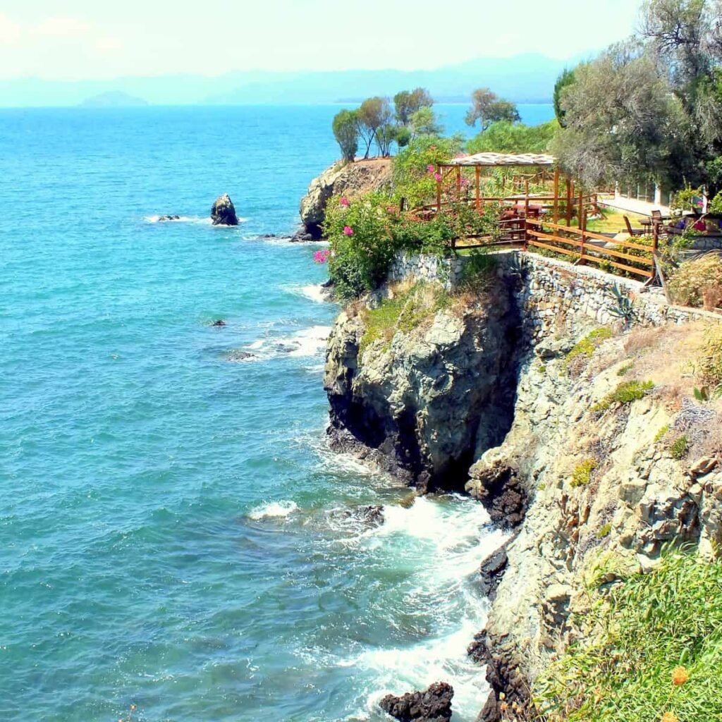 Sheer rock faces of Fethiye's Şövalye Island rise from the sea. A terrace is visible on top of the rocks and open sea is to the left.