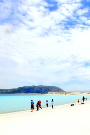 A cloudy sky over Salda, a crater lake with turquoise water. A handful of people line the shore.