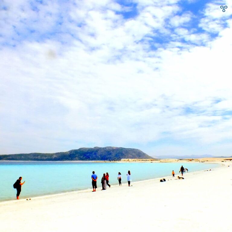 A cloudy sky over Salda, a crater lake with turquoise water. A handful of people line the shore.