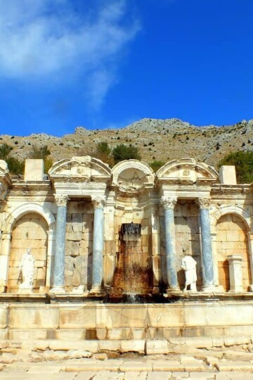 Sagalassos Antonine Nymphaeum - a long stone working fountain with water in the central area. Arches and columns line the fountain.