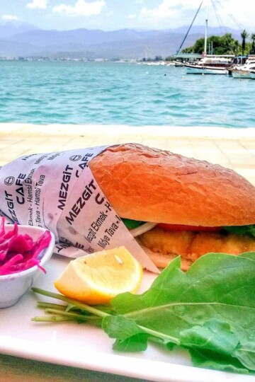 Battered fish in a crusty cob served with pickle, lemon wedge and rocket leaves. Fethiye harbour is in the background.
