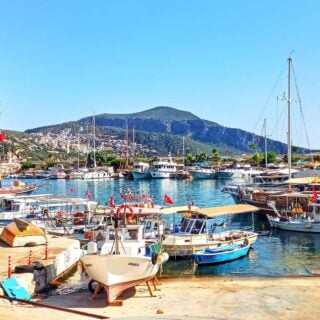 Kalkan harbour with small fishing boats in the foreground and larger wooden gulets anchored in deeper water.