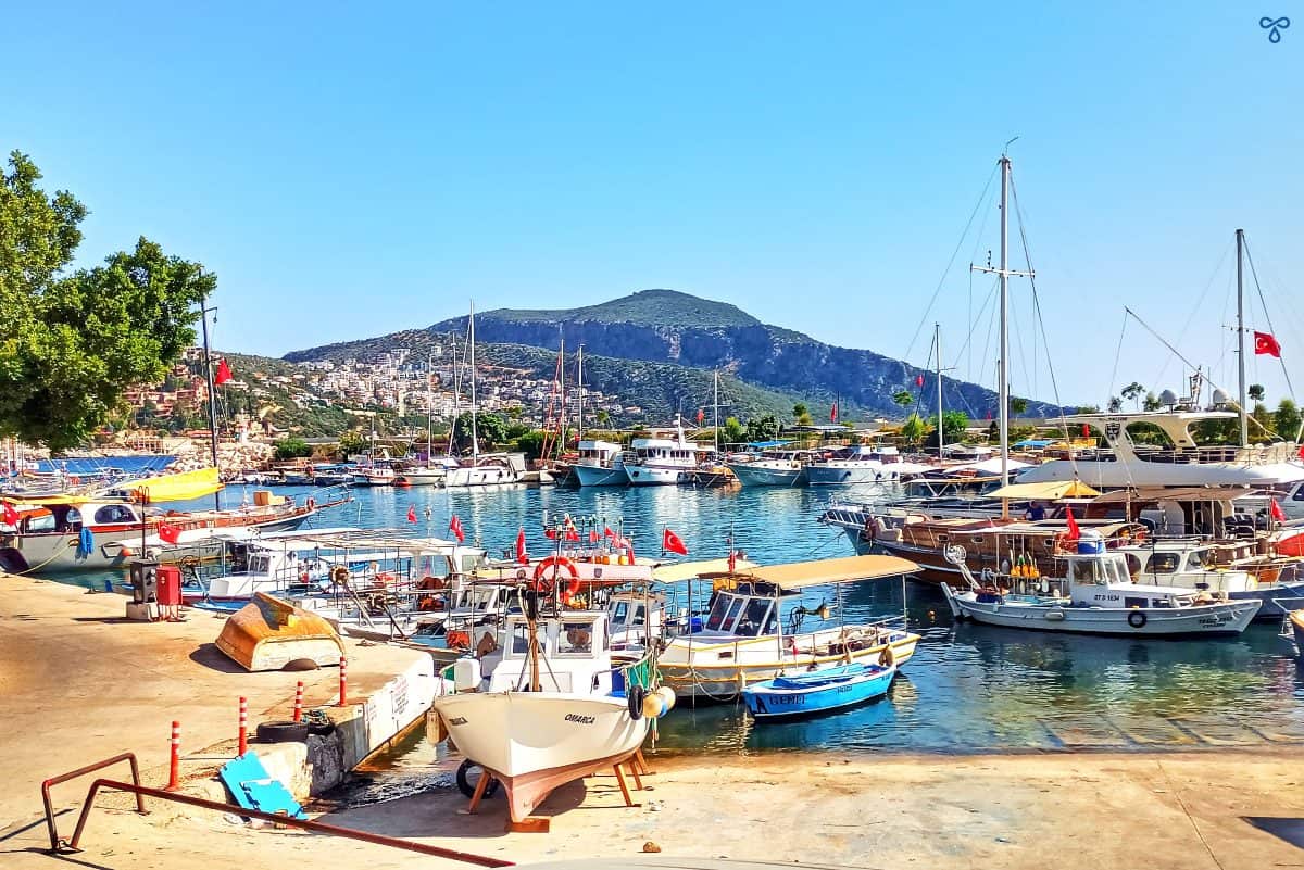Kalkan harbour with small fishing boats in the foreground and larger wooden gulets anchored in deeper water.