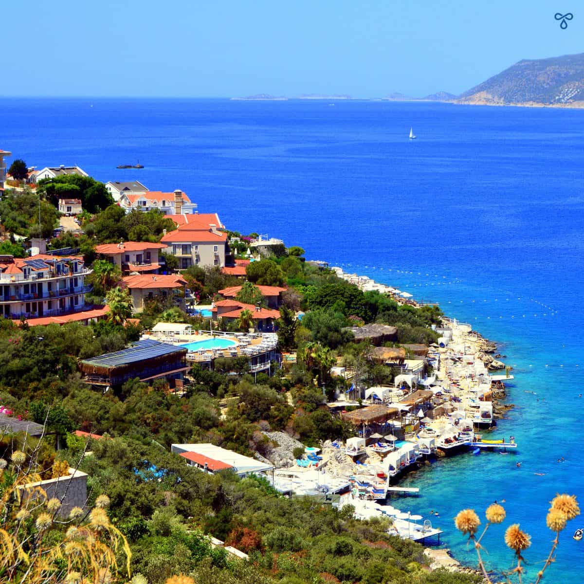 A view from above of the Kaş Peninsula coastline. Small bouıtique hotels are built up the tree-clad hillside and sunbathing platforms are around the shoreline.