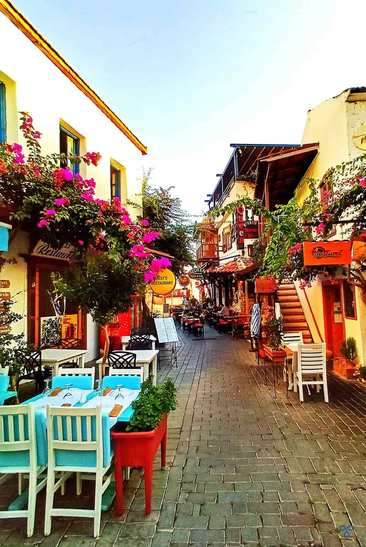 A narrow cobbled street in Kaş with restaurant tables along the left side. Bougainvillea grows up the side of the restaurant building.