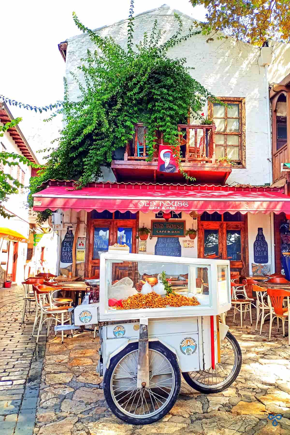 A street food cart piled with almonds over ice on a paved square in front of the Old House bar in Kaş.