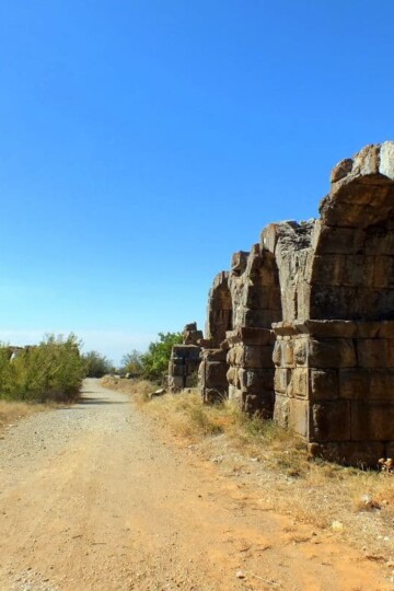 Stone Roman aqueduct arches curve round a dust track