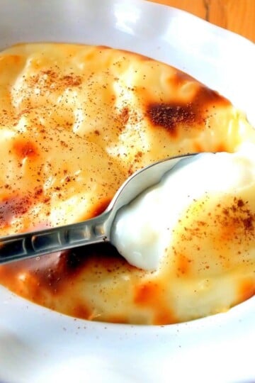 A spoon breaks through the skin of a bowl of sütlaç.