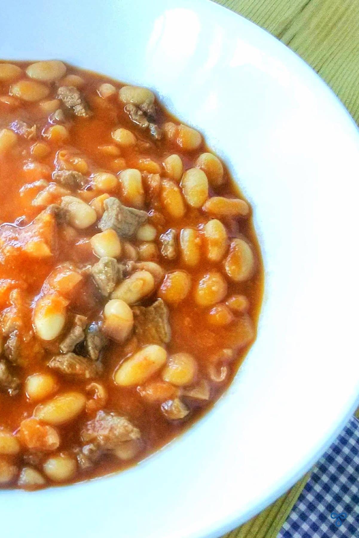 A close up of a bowl of kuru fasulye - a Turkish white bean stew where the beans are in tomato sauce. There are also small chunks of lamb in the bean stew.