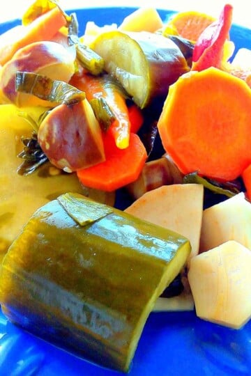A blue plate with mixed pickled vegetables on it. Green tomato, carrot, cucumber and aubergine.