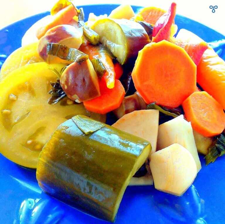 A blue plate with mixed pickled vegetables on it. Green tomato, carrot, cucumber and aubergine.