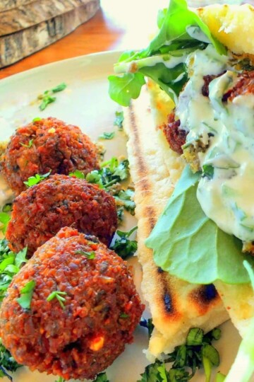 Three ball shaped falafel in a line. A flat bread is on the side, filled with falafel, yoghurt and rocket leaves.