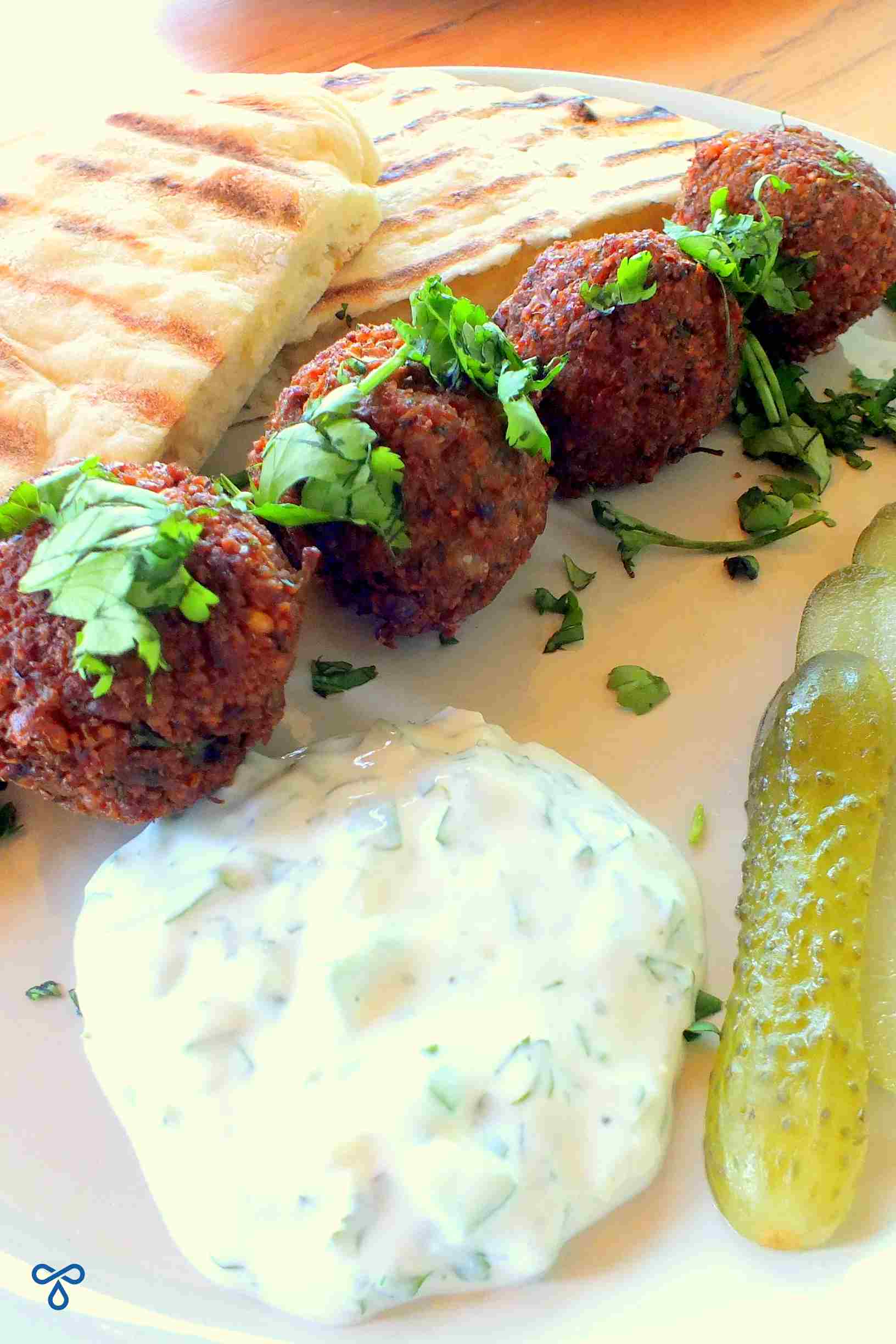 Four falafel balls served with pita bread and gherkins. A yoghurt sauce is on the plate in the foreground.