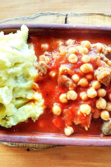 Turkish lamb and chickpea stew served in a rectangular clay pot with a side of mashed potatoes.