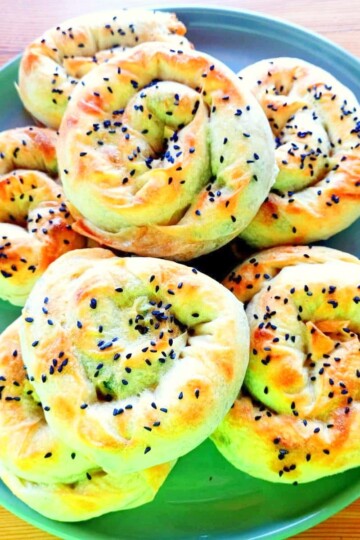 Seven rose pastry spirals - Turkish gül böreği - piled on a green plate. The cooked borek are topped with black nigella seeds.