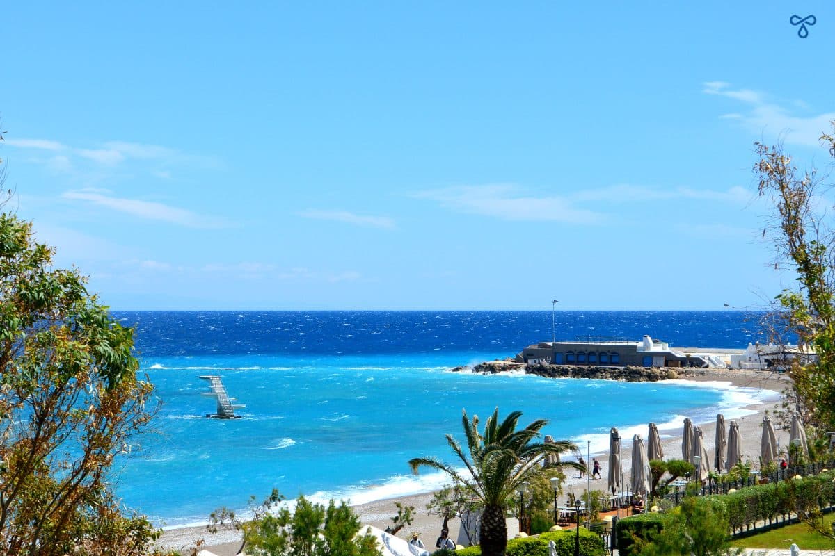 Elli Beach viewed from above on a windy day. The iconic diving board in the sea is visible.