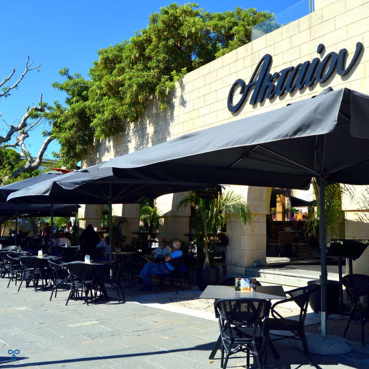Exterior of Aktaion Cafe. The name is written in large black lettering and big grey parasols shade the tables.