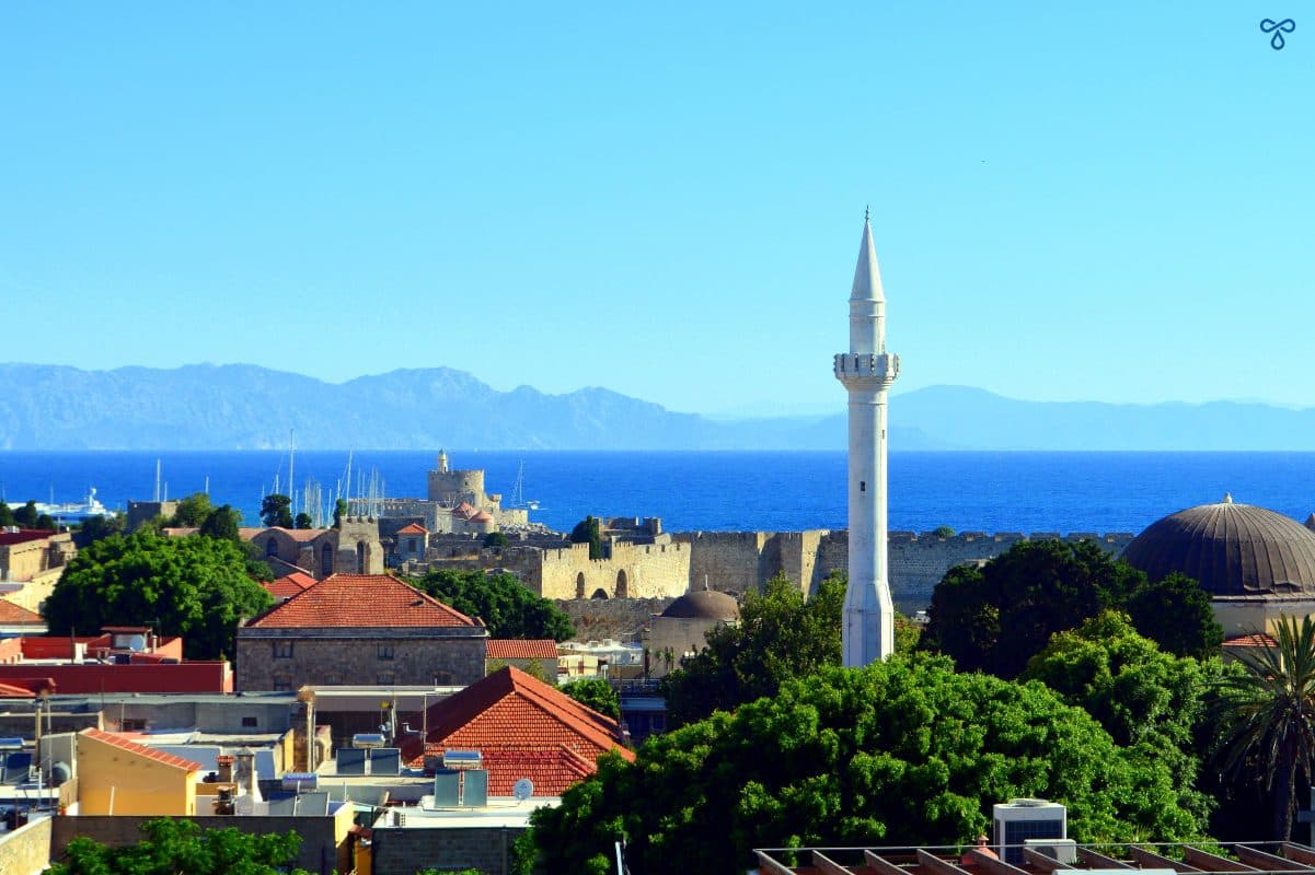 A view over the rooftops and out to sea in Rhodes Old Town from a roof terrace. A minaret dominates the skyline.