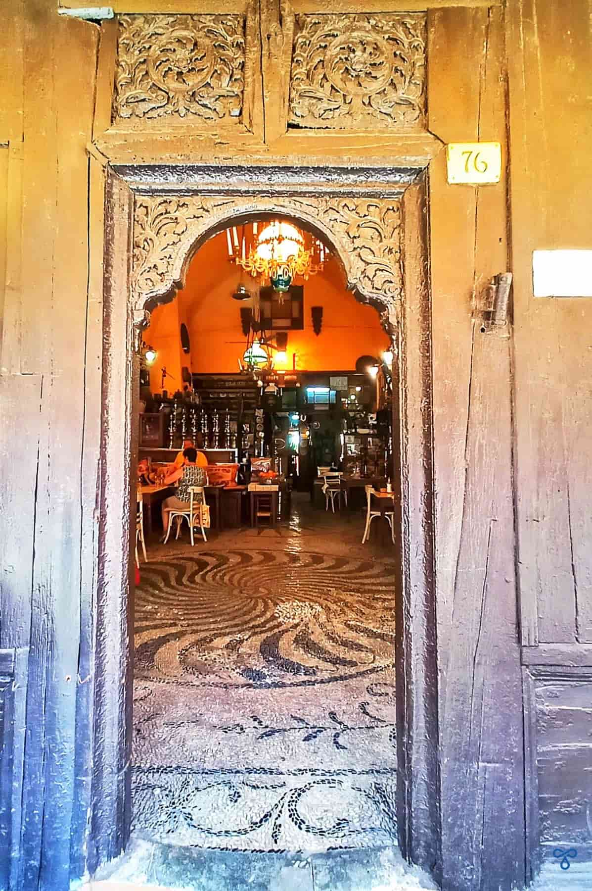 An old, ornate wooden doorway showing the interior of a bar with black and white pebbled floor.