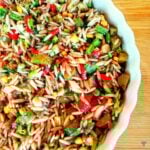 A bowl of orzo pasta salad taken from above. Red peppers, sweetcorn and chopped dill pickle are visible.