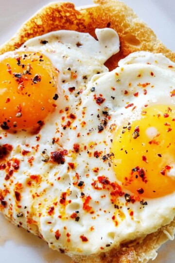 Two fried eggs topped with red chilli flakes. The eggs are on top of toasted bread.