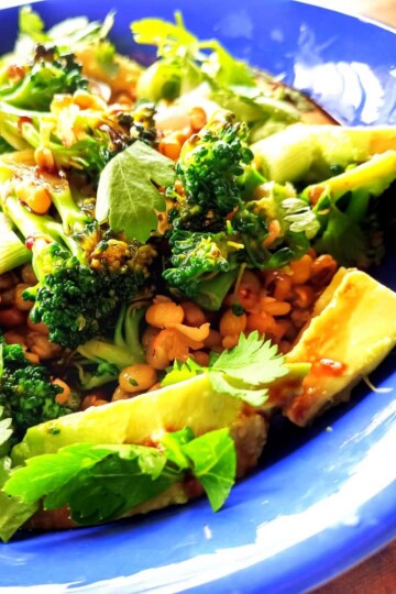 A circular blue bowl with mung beans, avocado slices, broccoli chunks and parsley leaves.