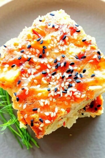 A slice of Turkish potato cake taken from above. The top is golden brown and sprinkled with nigella seeds and sesame seeds.