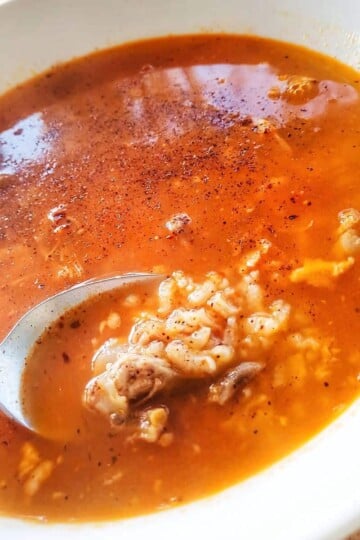 A square image of a spoon in a bowl of soup. The spoon is lifting out meat and rice.