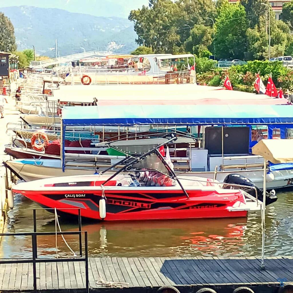 A red speedboat in the canal at Çalış. Other boats are also moored up behind it.