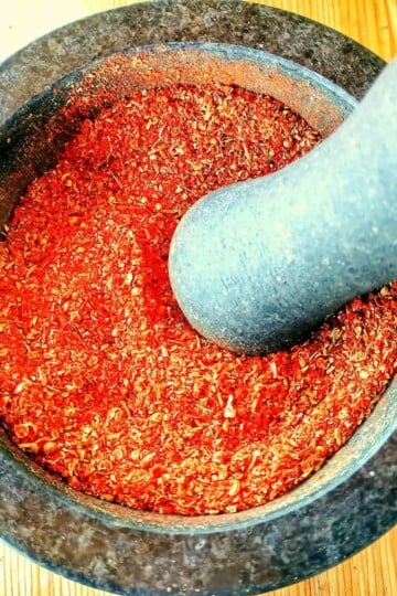 A granite pestle and mortar taken from above. It is filled with a red spice mix.