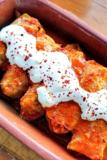 Five cabbage rolls in a rectangular clay dish, topped with natural yoghurt.