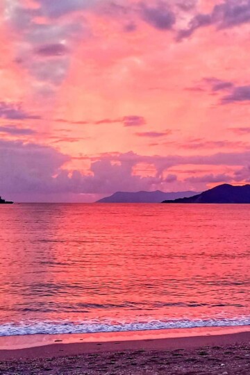 A pink sunset over Çalış Beach with silhouette of an island and a boat on the horizon.