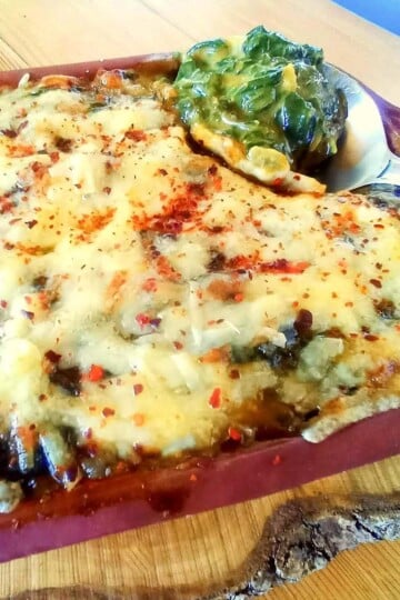 A close up of spinach gratin with a spoon scooping out some spinach from the corner of the dish.