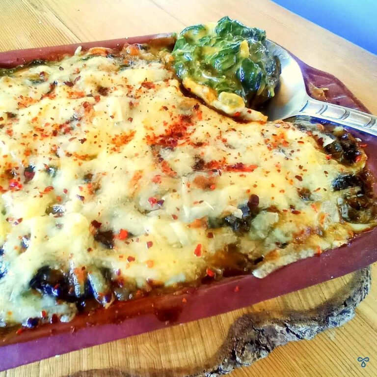 A close up of spinach gratin with a spoon scooping out some spinach from the corner of the dish.