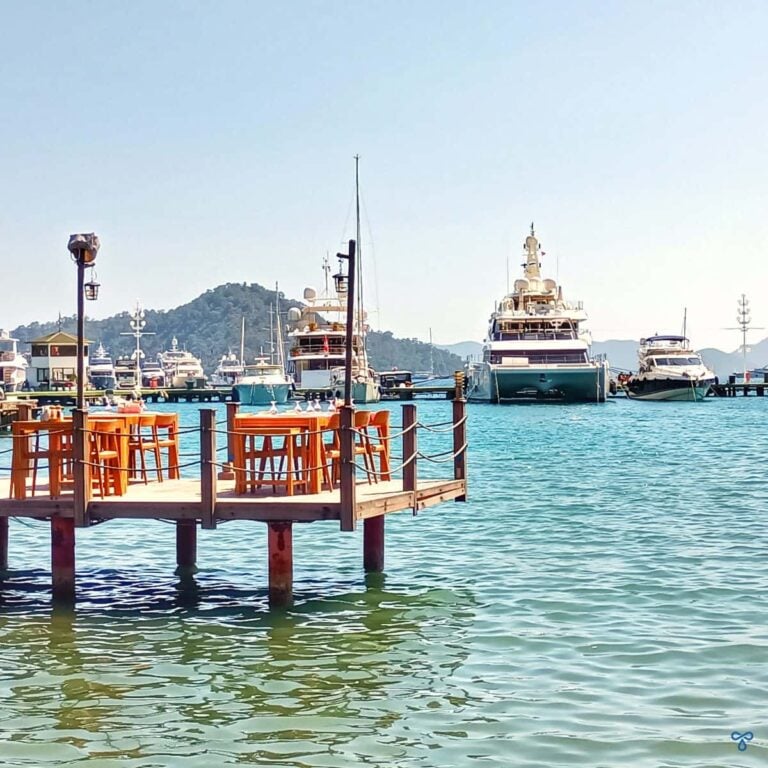 A jetty with tables and chairs overlooks super yachts in Göcek marina.