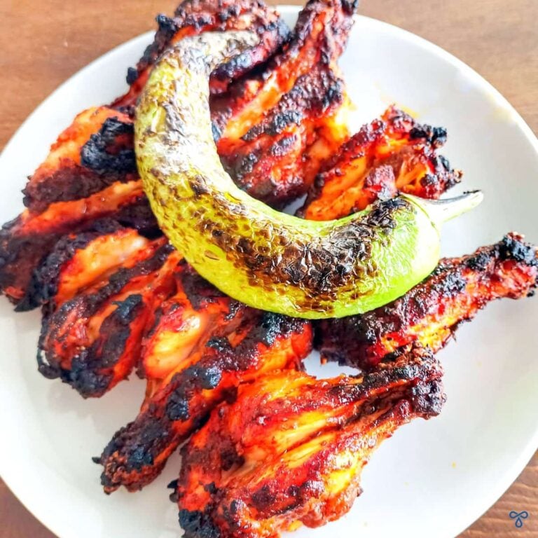 Eight barbecued chicken drumettes topped with a charred long green pepper.