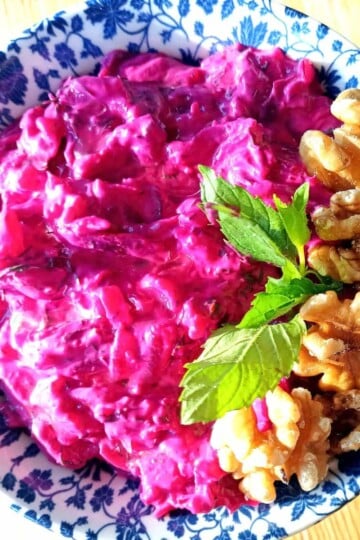 Beetroot yoghurt dip with a sprig of mint and walnuts on the side as a garnish.