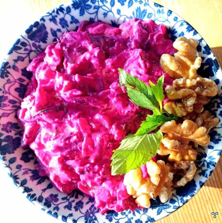 Beetroot yoghurt dip with a sprig of mint and walnuts on the side as a garnish.