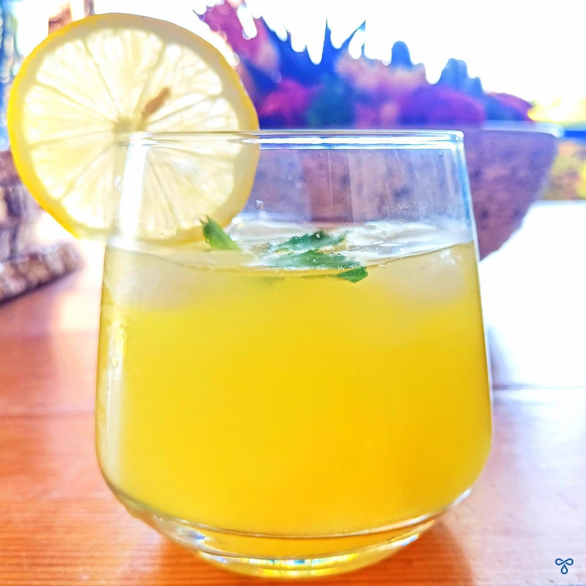 A glass of homemade Turkish lemonade with ice cubes and mint leaves. A slice of fresh lemon is on the edge of the glass.