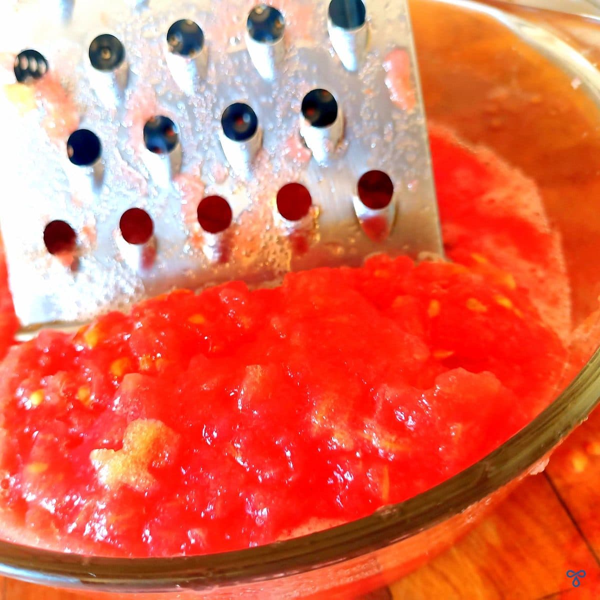 A box grater in a bowl of grated tomato pulp.