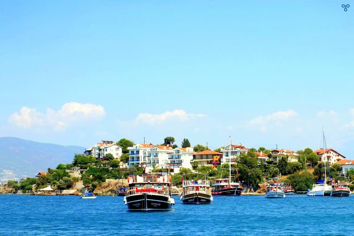 Fethiye day trip boats anchoring in front of Şövalye Island. Villas and trees are visible on the shoreline.