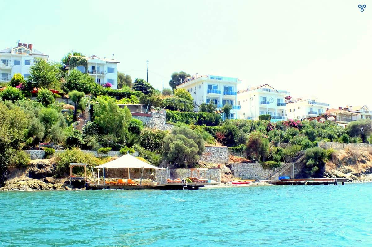 A tree clad hillside of Şövalye Island. Villas and a wooden bathing platform overlook the sea.