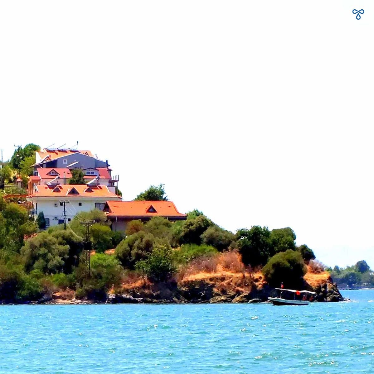 The tip of Şövalye Island with trees rising up the hillside and whitewashed villas at the top.