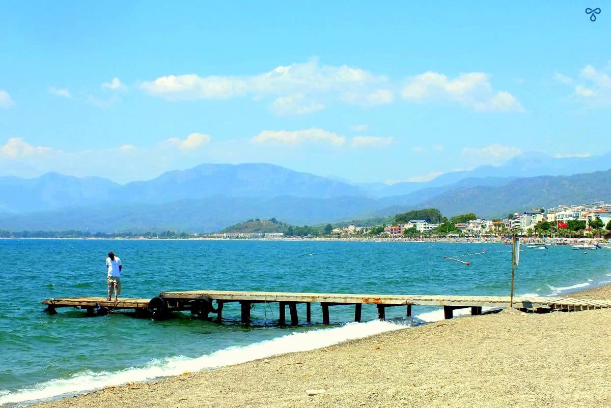 A wooden jetty on Çalış Beach going into the sea. A man is standing on the jetty. 