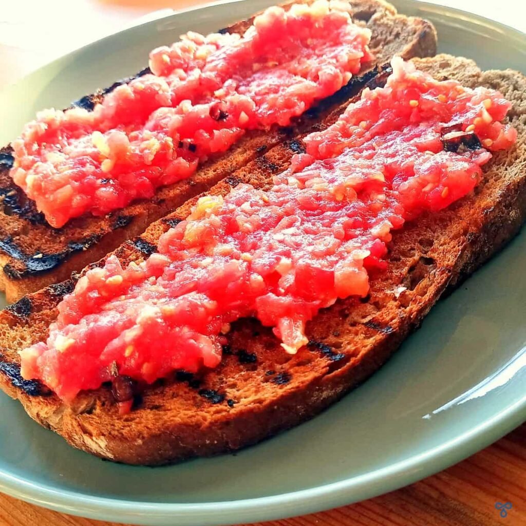Two slices of griddled brown bread topped with tomato pulp to make Spanish tomato bread.