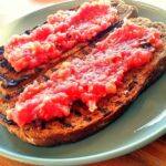 Two slices of griddled brown bread topped with tomato pulp to make Spanish tomato bread.