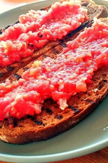 Two slices of griddled brown bread topped with tomato pulp to make Spanish tomato bread.