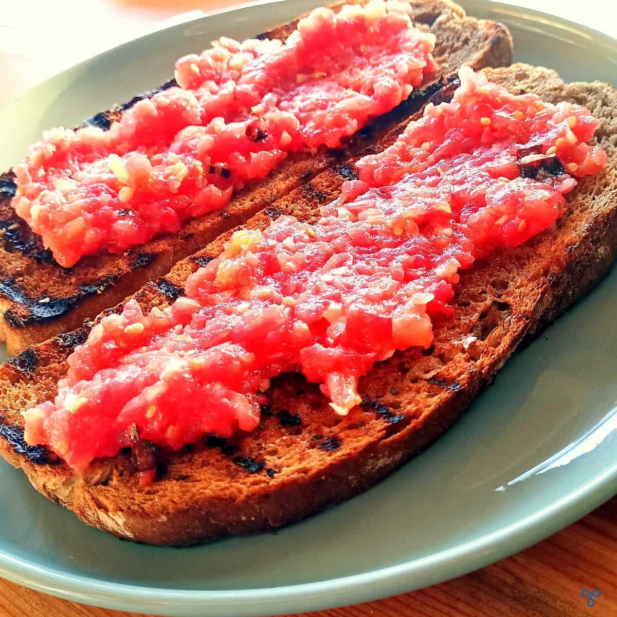Two slices of griddled brown bread topped with tomato pulp to make Spanish tomato bread.