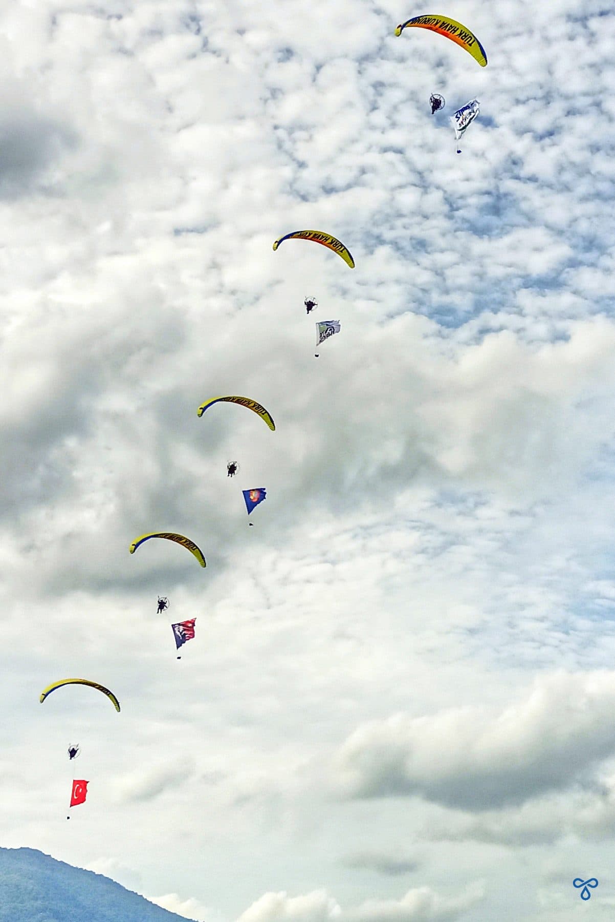 Five paramotors stacked in formation, gliding across a cloudy sky.